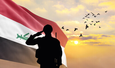 Silhouette of a soldier with the Iraq flag stands against the background of a sunset or sunrise....
