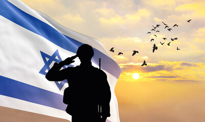 Silhouette of a soldier with the Israel flag stands against the background of a sunset or sunrise....