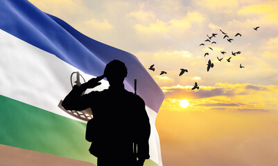 Silhouette of a soldier with the Lesotho flag stands against the background of a sunset or sunrise....