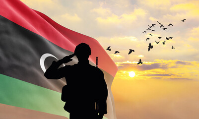 Silhouette of a soldier with the Libya flag stands against the background of a sunset or sunrise....