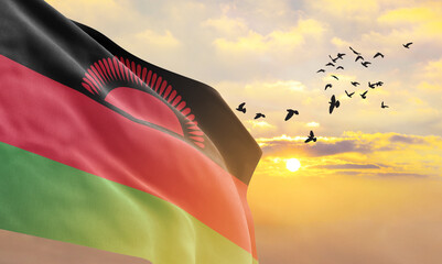 Waving flag of Malawi against the background of a sunset or sunrise. Malawi flag for Independence Day. The symbol of the state on wavy fabric. - obrazy, fototapety, plakaty