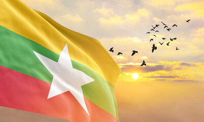 Waving flag of Myanmar against the background of a sunset or sunrise. Myanmar flag for Independence Day. The symbol of the state on wavy fabric. - obrazy, fototapety, plakaty