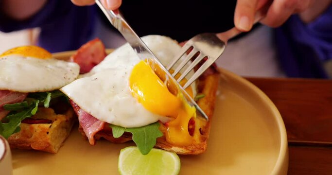 Close-up shot of sunny side up egg with its yolk elegantly cut by table knife. This enticing breakfast meal features mouthwatering combination: fried egg resting atop Belgian waffle