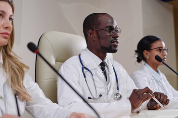 Doctor giving his speech at conference, while sitting at table with his colleagues