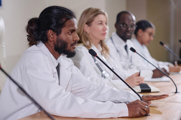 Group of doctors sitting in a row and giving an interview during press conference