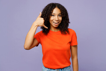 Little kid teen girl of African American ethnicity wear orange t-shirt doing phone gesture like says call me back isolated on plain pastel light purple background studio. Childhood lifestyle concept.