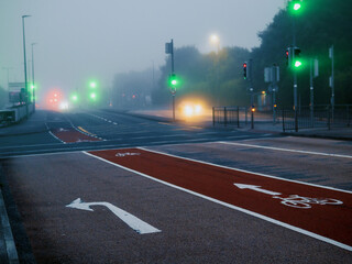Atmospheric empty road in the morning in a light fog. City way in a dusk. Selective focus. Bicycle path and traffic lights. Dark and moody look.