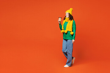 Full body side view young happy woman wear green knitted sweater yellow hat scarf hold takeaway...