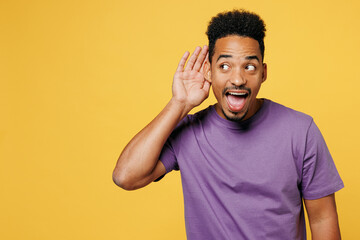 Young nosy man of African American ethnicity he wears purple t-shirt casual clothes try to hear you overhear listening intently isolated on plain yellow background studio portrait. Lifestyle concept.
