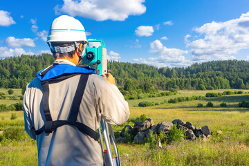 Man surveyor with his back to camera. Guy with geodetic instrument near forest. Surveyor takes...