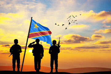 Silhouettes of soldiers with the DR Congo flag stand against the background of a sunset or sunrise....