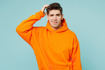 Young shocked sad upset man he wears orange hoody casual clothes look camera scratch hold head look...