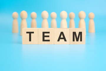 the term - TEAM - is inscribed on wooden cubes on a bright blue background. wooden figures of...