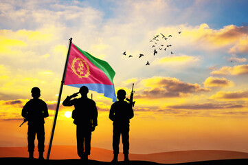 Silhouettes of soldiers with the Eritrea flag stand against the background of a sunset or sunrise....