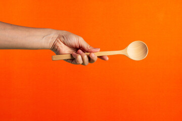 Spoon wooden in hand on orange background - obrazy, fototapety, plakaty