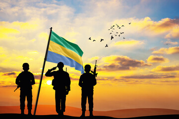 Silhouettes of soldiers with the Gabon flag stand against the background of a sunset or sunrise. Concept of national holidays. Commemoration Day.