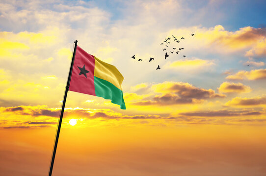 Waving flag of Guinea-Bissau against the background of a sunset or sunrise. Guinea-Bissau flag for Independence Day. The symbol of the state on wavy fabric.