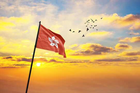Waving flag of Hong Kong against the background of a sunset or sunrise. Hong Kong flag for Independence Day. The symbol of the state on wavy fabric.
