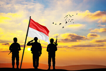 Silhouettes of soldiers with the Indonesia flag stand against the background of a sunset or...