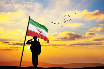 Silhouette of a soldier with the Iran flag stands against the background of a sunset or sunrise....