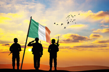 Silhouettes of soldiers with the Ireland flag stand against the background of a sunset or sunrise....