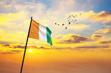 Waving flag of Ivory Coast against the background of a sunset or sunrise. Ivory Coast flag for...