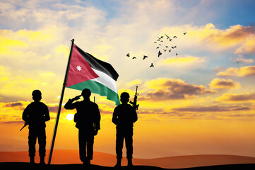 Silhouettes of soldiers with the Jordan flag stand against the background of a sunset or sunrise....