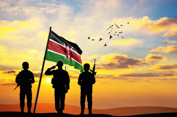 Silhouettes of soldiers with the Kenya flag stand against the background of a sunset or sunrise....