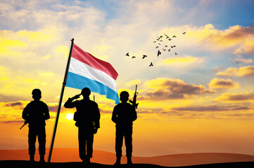 Silhouettes of soldiers with the Luxembourg flag stand against the background of a sunset or sunrise. Concept of national holidays. Commemoration Day.