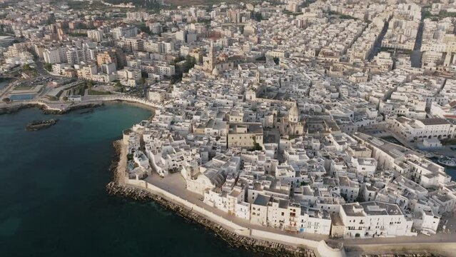 Wide aerial rotating footage of the town of Monopoli, Italy in the light of the sunrise and the blue water of the Mediterranean.