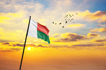 Waving flag of Madagascar against the background of a sunset or sunrise. Madagascar flag for Independence Day. The symbol of the state on wavy fabric.