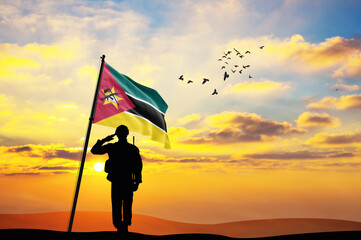 Silhouette of a soldier with the Mozambique flag stands against the background of a sunset or...