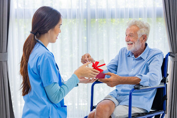 Hospice nurse is giving christmas present to Caucasian man in the wheelchair in pension retirement center for home care rehabilitation and post treatment recovery process