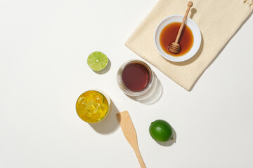 On a white background, a jar of honey, honey drizzle, fresh lemon, and a glass of honey kumquat tea form a health-conscious tableau. Embracing the goodness of natural products in healthcare.
