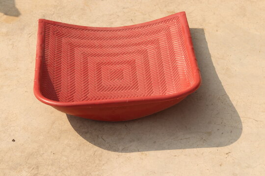 A red colored rice cleaner or soop, supa ,muram or moram on floor in sunlight, back shot