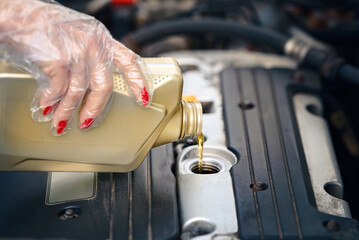 Woman check oil level and top up engine oil. Female hand in protective gloves pouring motor oil....