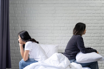 Sad or depressed woman sitting on bed with her couple. Lesbian couple relation problem concept - obrazy, fototapety, plakaty