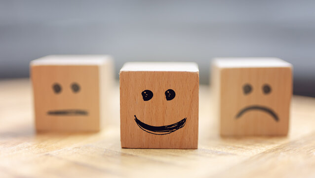 Wooden cubes with a happy face in front and sad ones in the background.