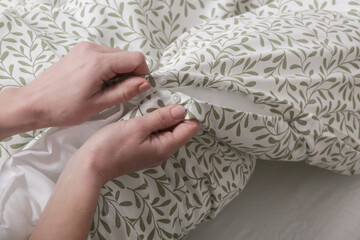 Woman is closing buttons on duvet cover while making the bed, close up
