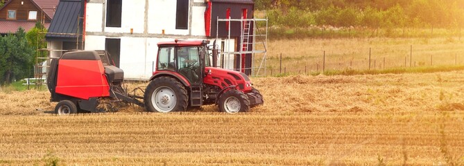 A red tractor and its attached machinery work diligently to harvest the golden crops under the warm...
