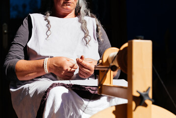Unrecognizable senior woman spinning wool on machine on sunny day