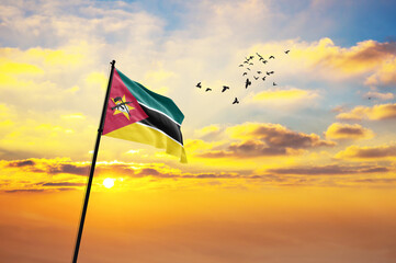 Waving flag of Mozambique against the background of a sunset or sunrise. Mozambique flag for...