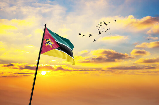 Waving flag of Mozambique against the background of a sunset or sunrise. Mozambique flag for Independence Day. The symbol of the state on wavy fabric. - Powered by Adobe