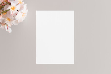 White invitation card mockup with a oleander on the beige table. 5x7 ratio, similar to A6, A5.