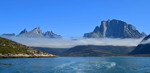 rugged mountain peaks and low-lying clouds near the sermeq glacier 
 at the end of the tasermuit fjord on a sunny summer day near nanortalik, in southern greenland