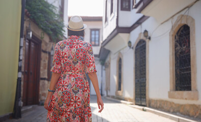 Fototapeta premium female summer travel to Antalya, Turkey. young asian woman in red dress walk through old town Kalechi , female tourist traveler discover interesting places and popular tourist attraction