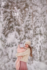 Winter. Snow. Mom and baby in the winter forest. Portrait. Mom gently holds her daughter in her arms. The baby is wrapped in a warm blanket. Trees in the snow. Family. Mom and daughter. Cold. Snowy