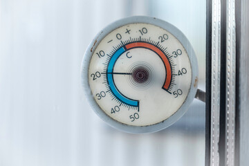 Circular old outdoor thermometer with minus 20 degrees celsius hangs on the outside of the window