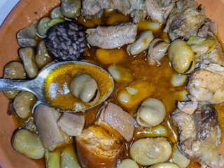 Spoon with broad beans in sauce on a plate of typical broad beans with pork ribs and sausages