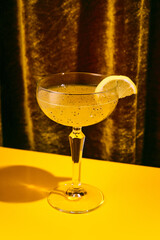 Close up photo of exotic alcohol drink in tall glass with wide mouth garnished with piece of orange sitting on yellow table. Concept of party time, restaurant, holidays, Valentines Day, celebration.